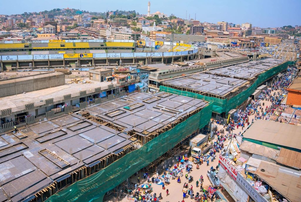 “Nakivubo Bridge construction progress showing concrete deck works, commercial block development, and busy market activity in downtown Kampala.”